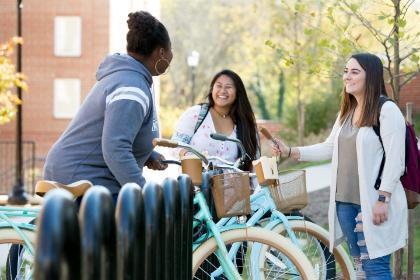 Three students talk around a bicycles rack.