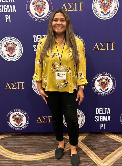 Karla Grijalva Lopez standing in front of Delta Sigma Pi step and repeat banner.