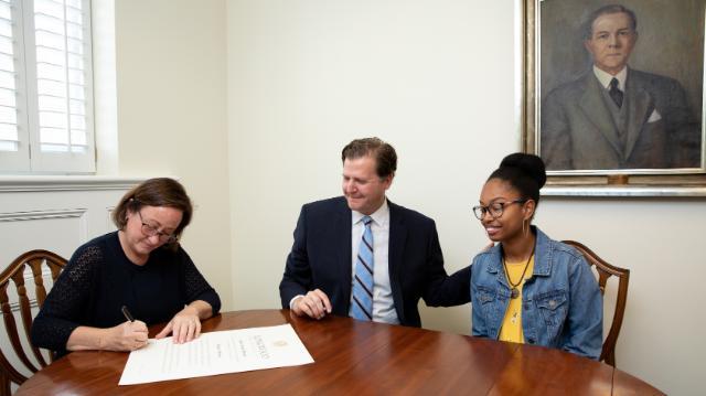Chaniece Williams ‘19 and President W. Taylor Reveley IV watch as Marianne Radcliff ’92, rector of the Board of Visitors, signs Williams’ Longwood diploma last month.