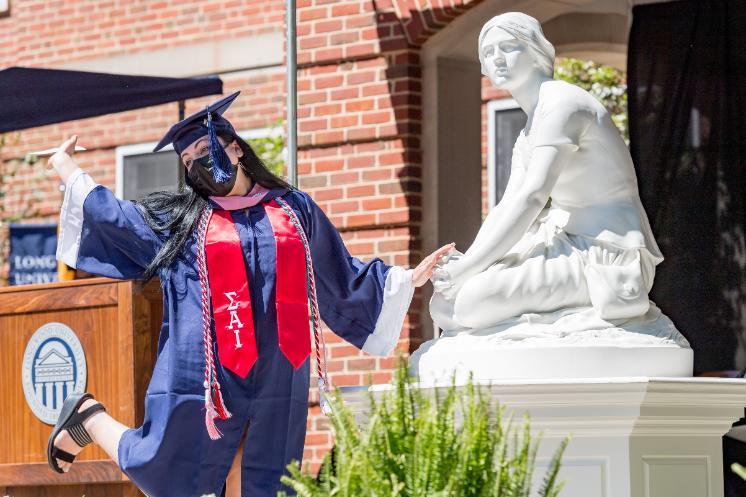 Student kicks up her heels while touching Joanie's hand on the Commencement stage