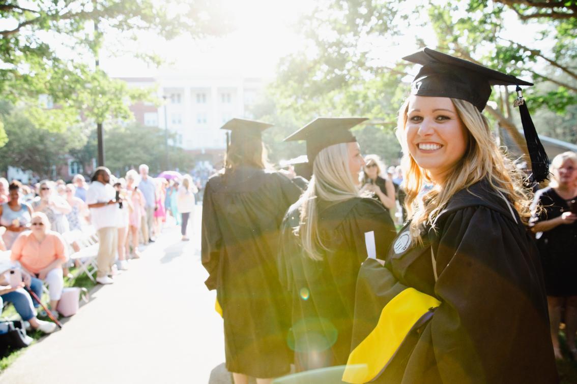 Graduate student looks back at the photographer with sun bursting behind her